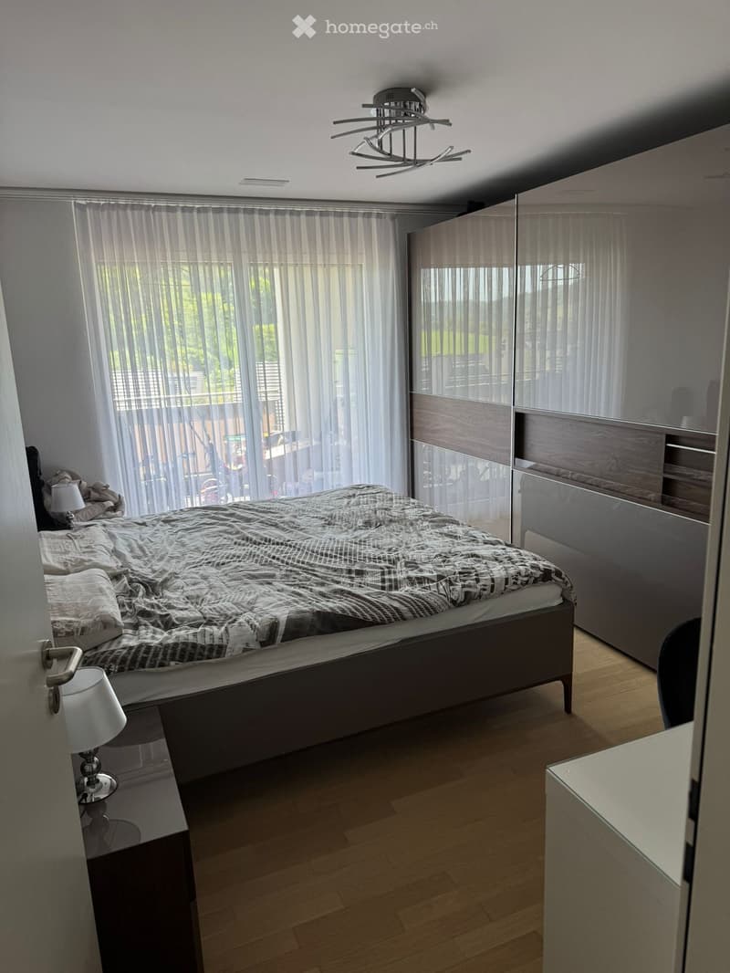 Modern bedroom with wooden flooring, large bed with patterned bedding, nightstand with lamp, and a tall wardrobe with mirrored doors.