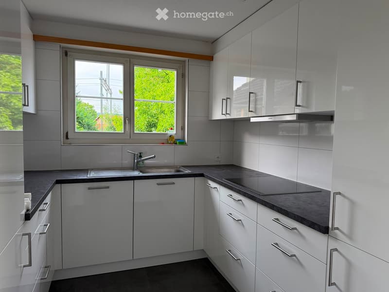 Modern kitchen with white cabinets, dark countertops, stainless steel sink, and range hood. Large window provides natural light.