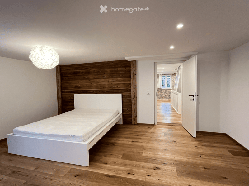 Spacious bedroom, wooden bed, wooden wall, hardwood flooring, white ceiling with light fixtures, open door leading to hallway