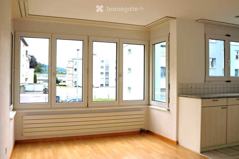 Empty room with wooden flooring, large windows, radiator, and white cabinets.