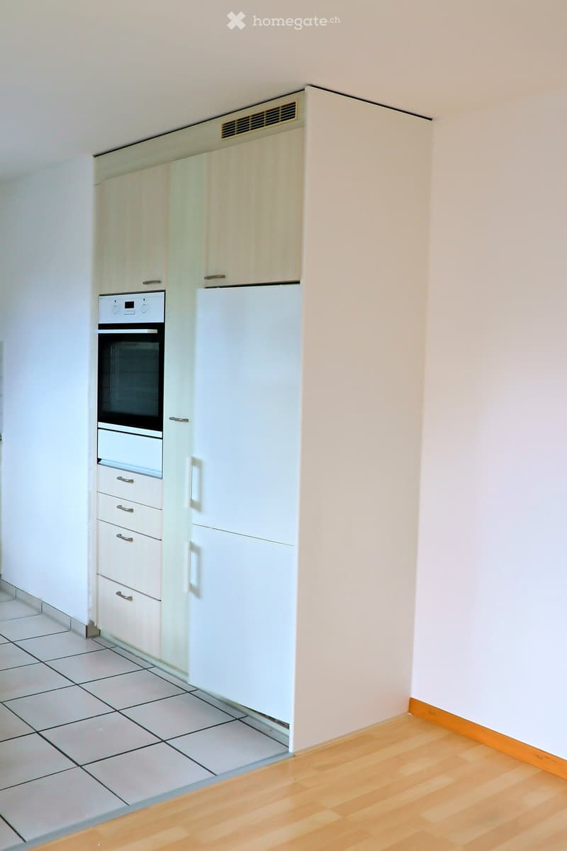 Modern kitchen with white cabinets, a refrigerator, and an oven. The floor is tiled in one area and wooden in another.