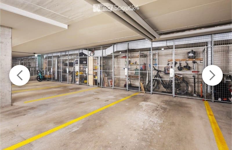 Underground garage with concrete floor, yellow parking lines, metal storage cages, bicycles, and tools.