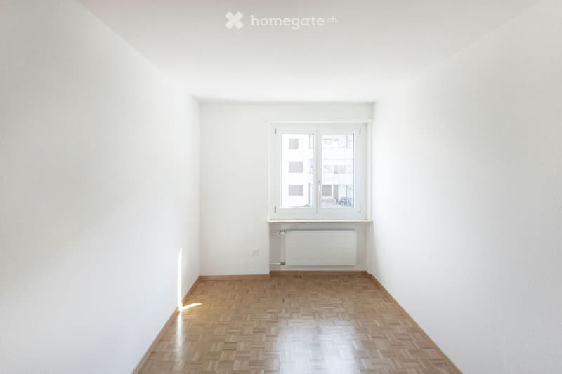 Completely empty room with white walls, wooden floor, and a single window with a radiator below it.