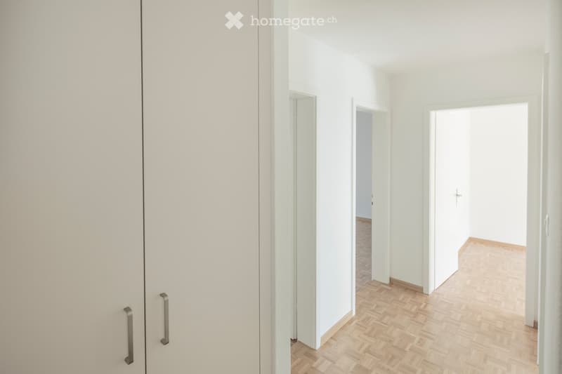 Empty hallway with white walls, wooden flooring, and several open doors leading to other rooms.