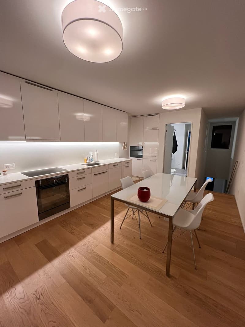 Modern kitchen with white cabinets, wooden flooring, and a dining area featuring a glass table and white chairs.