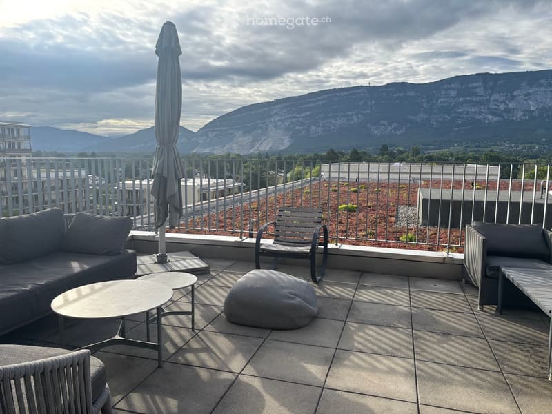 Balcony with a sofa, coffee table, ottoman, chairs, and an umbrella, overlooking a scenic mountain view.