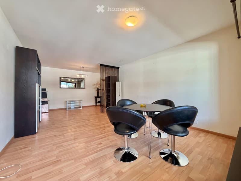 Modern dining area with wooden flooring, round table with four black chairs, wall-mounted mirror, and built-in cabinetry.
