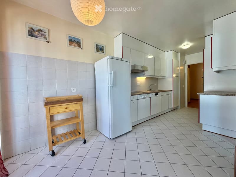 Modern kitchen with white cabinets, a refrigerator, dishwasher, and a wooden cart with wheels.