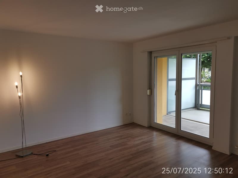 empty room with wooden floor, white walls, floor lamp, sliding glass door leading to balcony