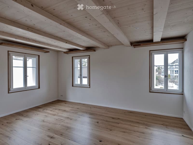 large room, wooden floors, exposed wooden beams, two large windows