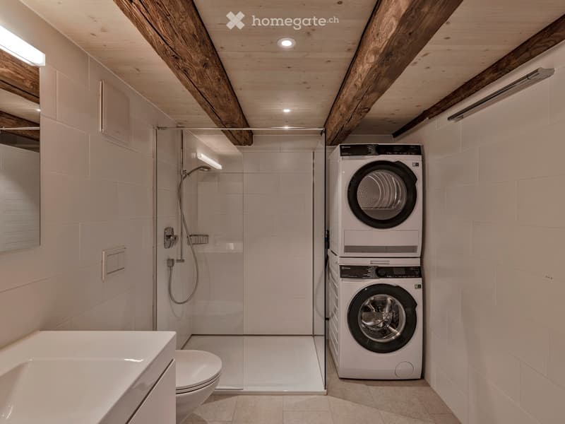 Private bathroom with a shower, a toilet, a sink, and a stack of a washing machine and a dryer