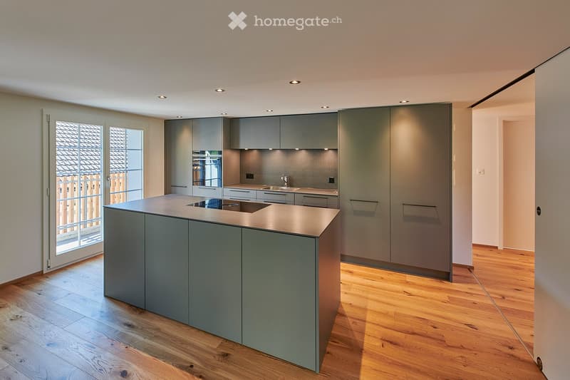 Modern kitchen with grey cabinets, a central island, and a sink, featuring wooden flooring and recessed lighting.
