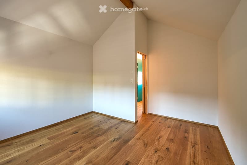 Empty room with wooden flooring and white walls, featuring a slanted ceiling and an open doorway leading to another room.