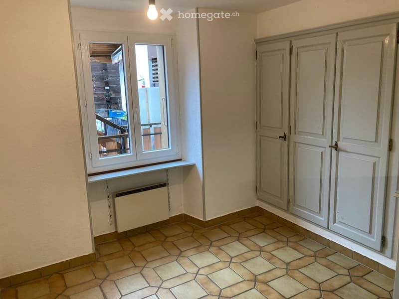 Empty room with beige tiled floor, white walls, built-in cabinets, and a window opening to a balcony area.