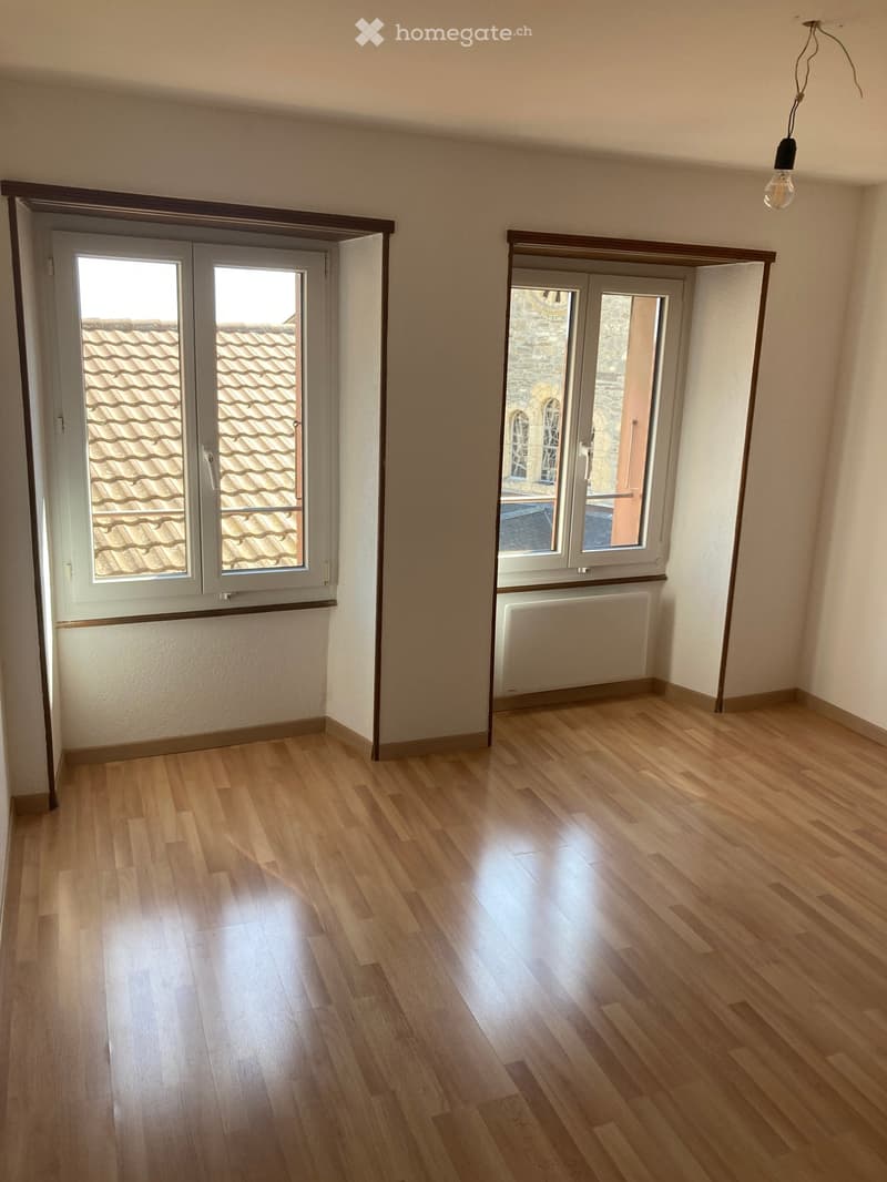 Empty room with wooden flooring, large windows, and a radiator visible in the background.