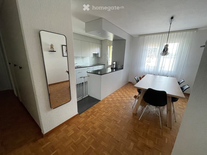 Open-plan living and dining area with a modern kitchen, wooden flooring, a large mirror, and a dining table with chairs.