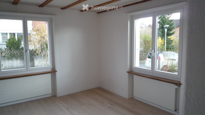 Empty room with wooden flooring, white walls, large windows, and radiators beneath the windows.