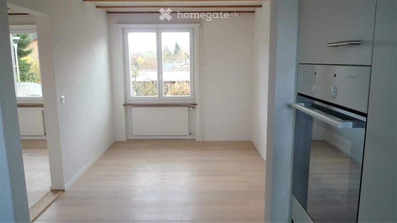 Empty room with light wooden flooring, white walls, and large windows. No furniture or equipment present.
