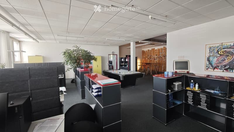 Office space with multiple desks, chairs, computer monitors, keyboards, filing cabinets, a plant, and a pool table in the background.