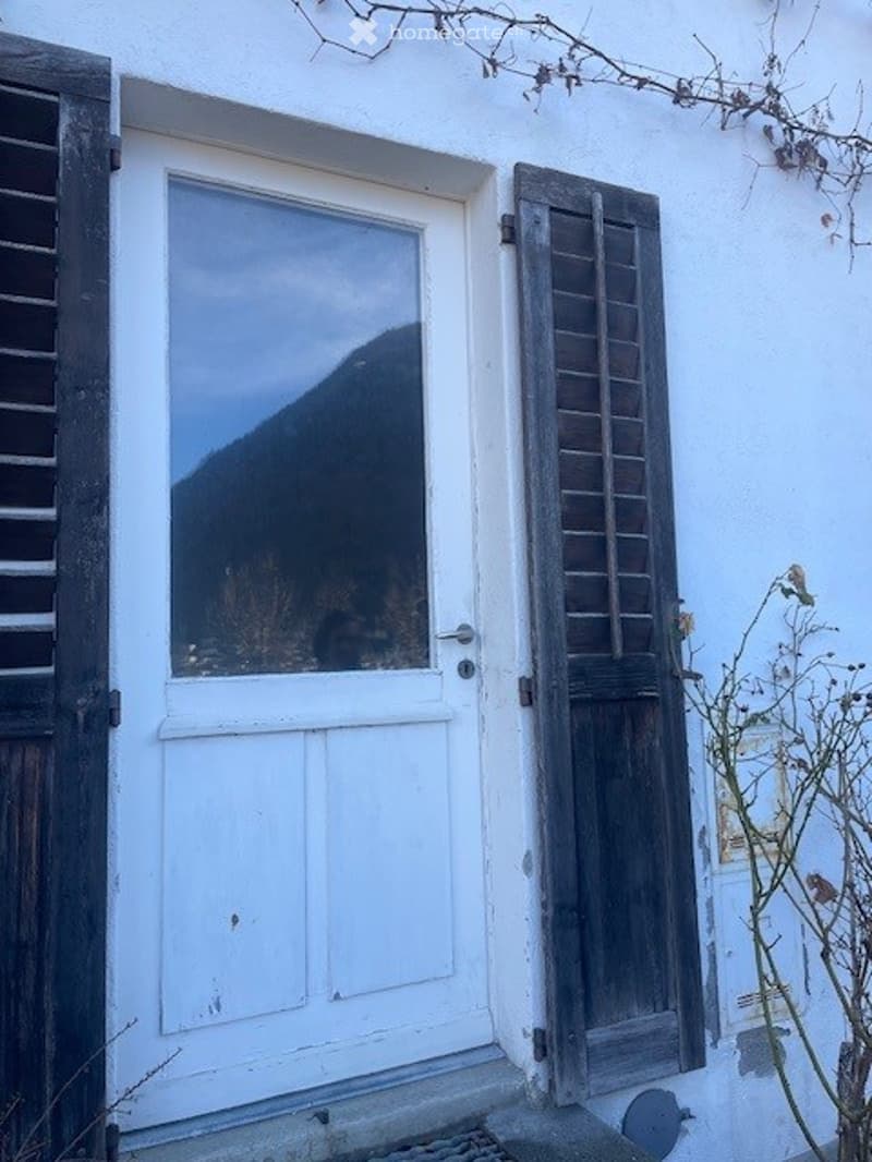 White exterior door with glass panel, wooden shutters, and a view of a mountain through the glass.