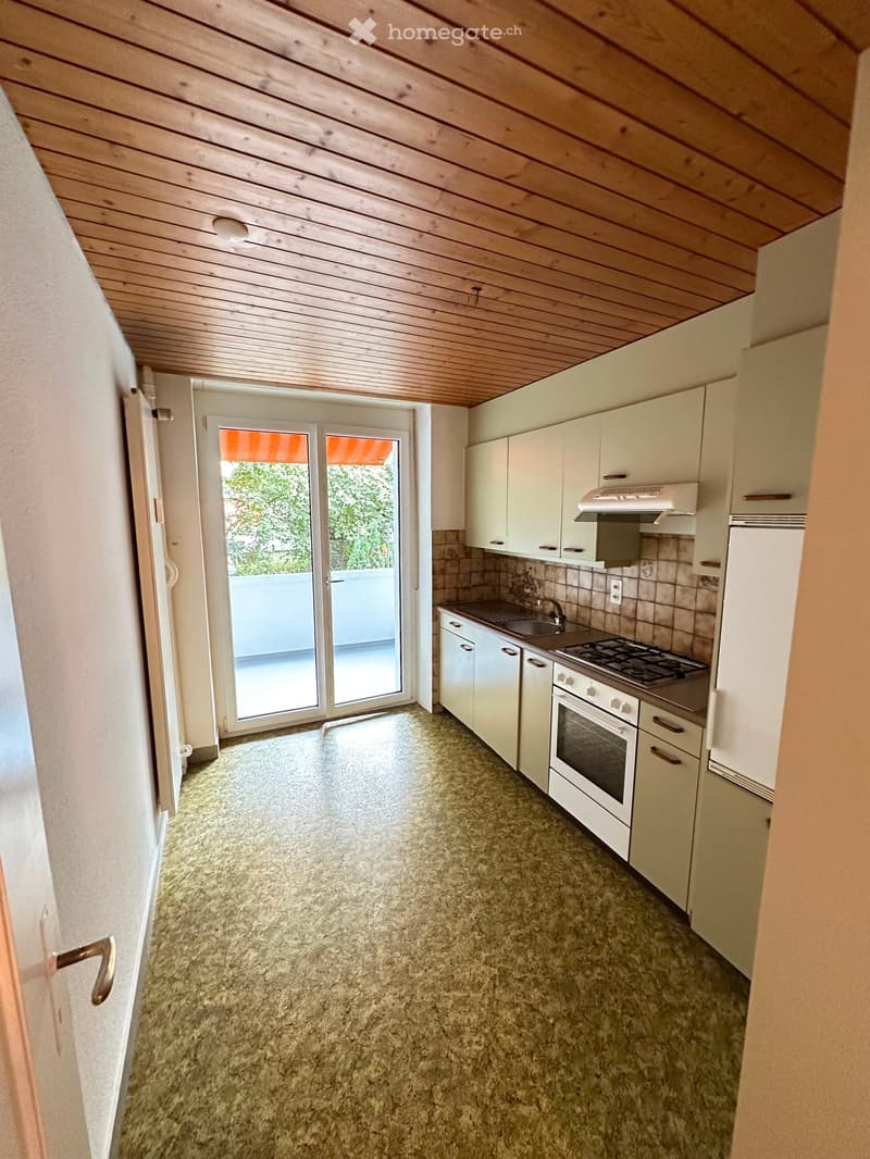 Bright kitchen with white cabinets, a stove, oven, sink, and a sliding glass door leading to a balcony.
