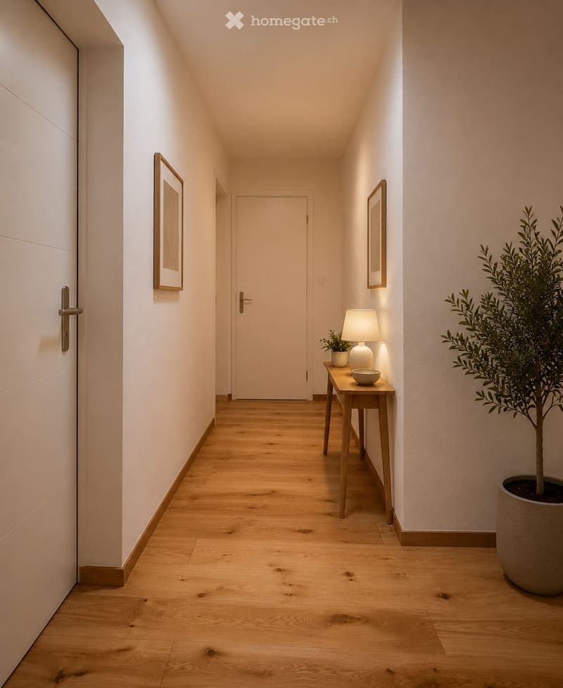 Modern hallway with light wooden flooring, white walls, and subtle lighting. Features a small wooden console table with a lamp, bowl, and potted plant, along with framed artwork on the walls.