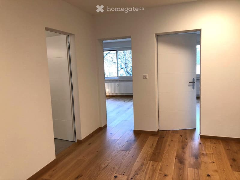 Empty hallway with wooden flooring, white walls, and two doors leading to other rooms.