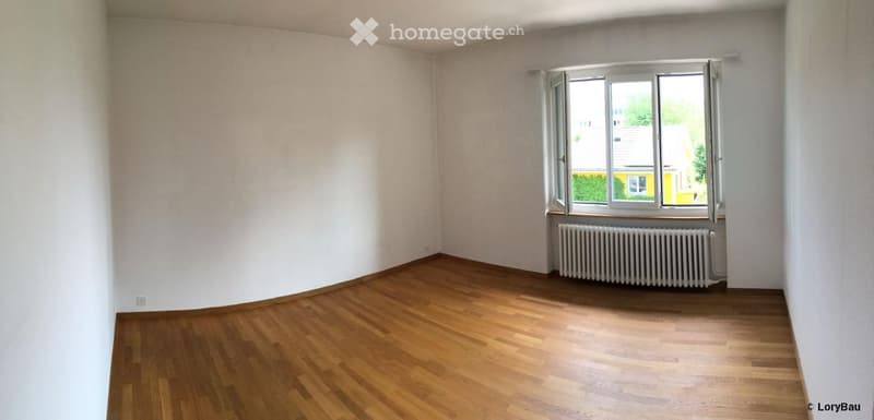 Empty room with wooden flooring, white walls, and a large window with a radiator below it.
