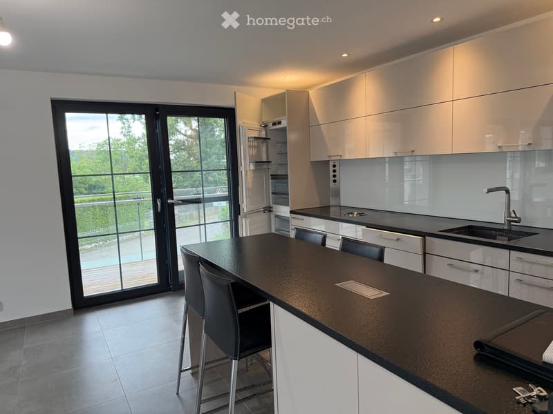 Modern kitchen with white cabinets, black countertops, bar stools, and a large window offering a view of the outdoor area.