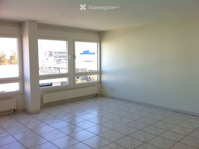 Empty room with tiled floor, white walls, large windows, and radiators along the walls.
