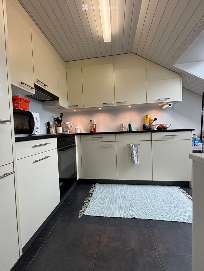 Modern kitchen with white cabinets, black countertops, and stainless steel appliances. Features include a microwave, oven, dishwasher, and various kitchen items on the counter.