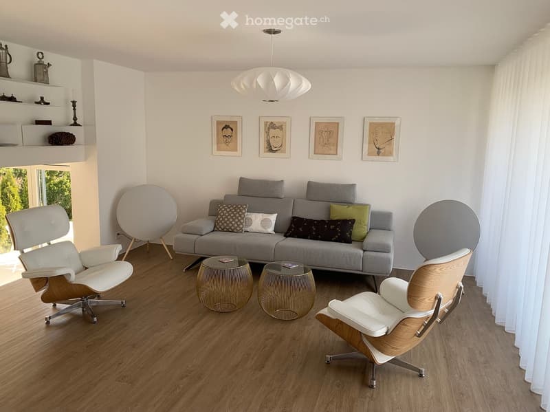 Modern living room with a grey sofa, two white chairs, two round tables, a hanging lamp, and a shelf with decorative items.
