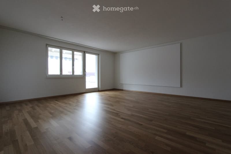 Empty room with wooden flooring, large window, and sliding glass door leading outside.