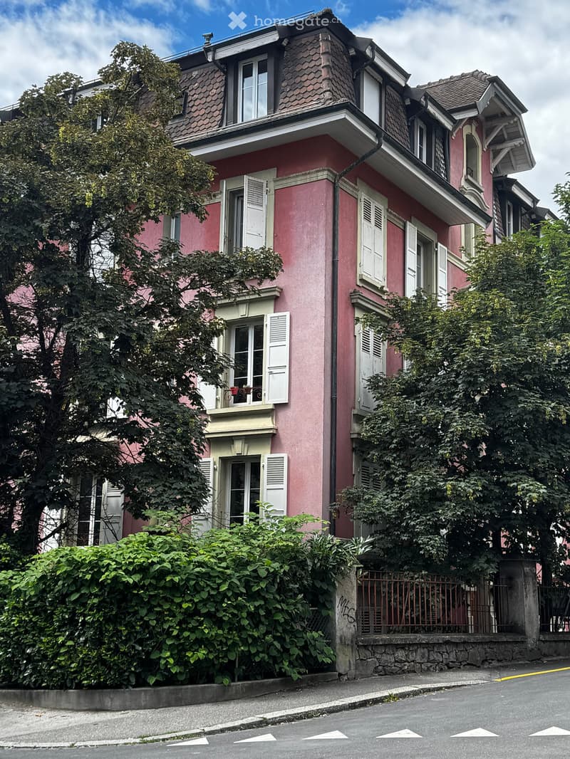 Pink multi-story house with white shutters, multiple windows, and a small balcony with potted plants.