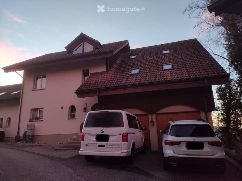 Two-story house with a tiled roof, garage, and two parked vehicles in front.