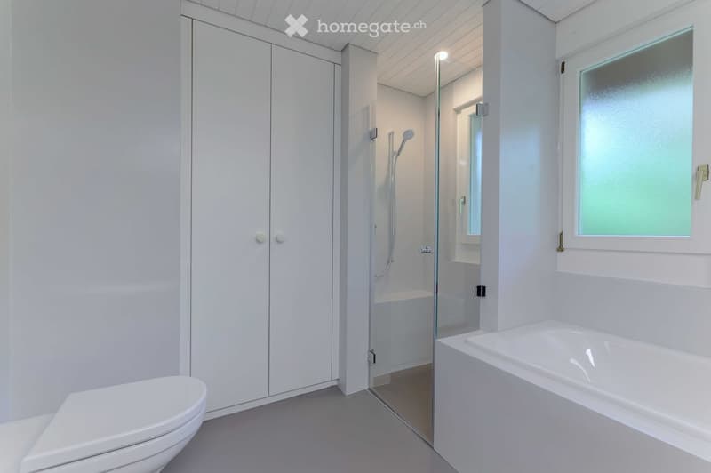 modern bathroom with white walls, white bathtub, white toilet, glass shower enclosure, white cabinets