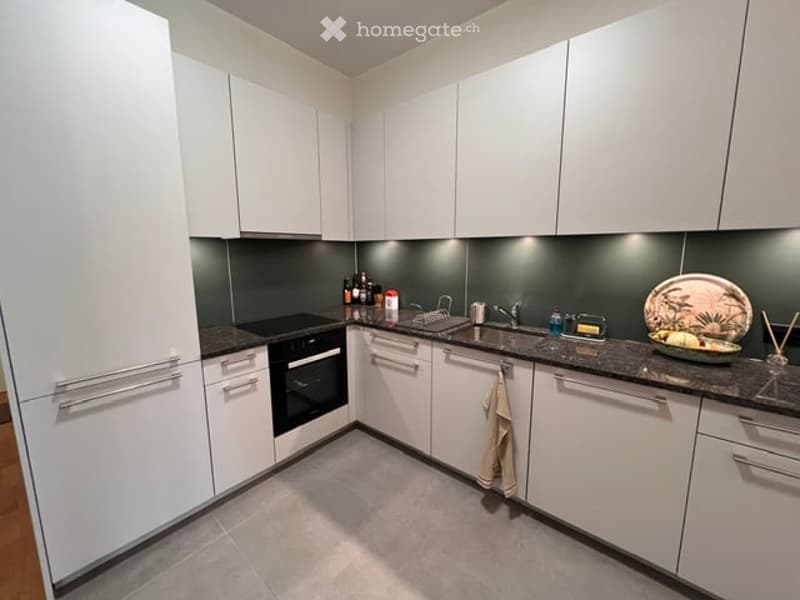Modern kitchen with white cabinets, dark countertops, built-in oven, sink, and various small appliances and items on the counter.