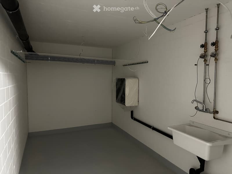 Utility bathroom with white tiled walls, a metal shelf, a sink with a faucet, and exposed pipes.