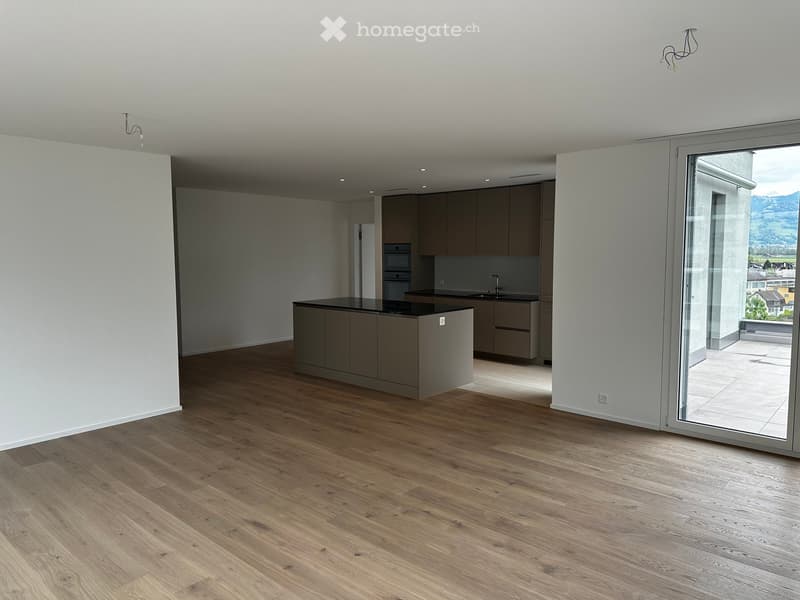 Modern kitchen with light wood flooring, grey cabinets, a central island, and a large sliding glass door leading to a balcony.