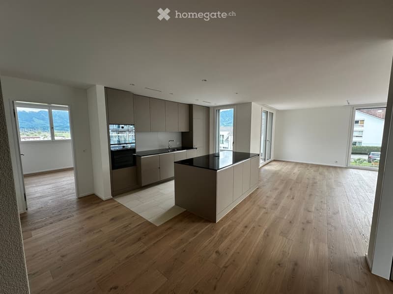 Modern kitchen with light wood flooring, grey cabinets, a central island, and large windows offering a mountain view.
