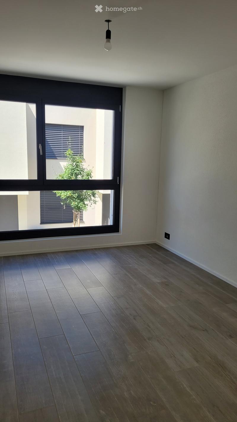 Empty room with wooden flooring, large window with blinds, and a single hanging light fixture.