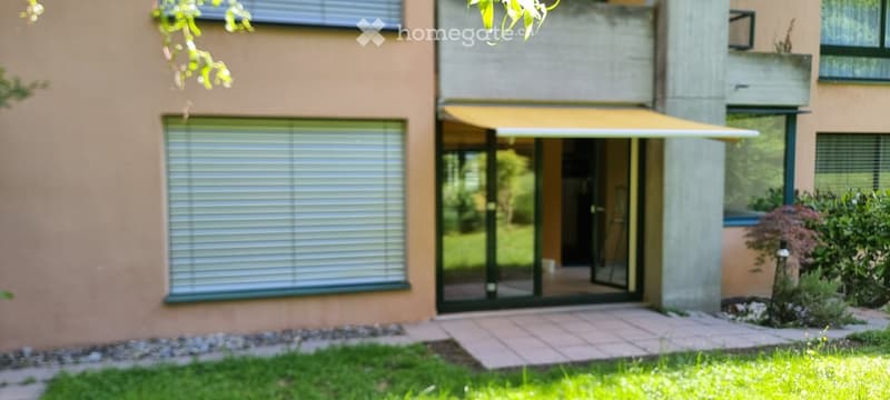 Building. Modern building entrance with large glass sliding doors, covered awning, and small garden area.