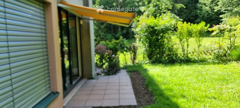 A pathway leads from a house to a lush green garden area with trees and shrubs.