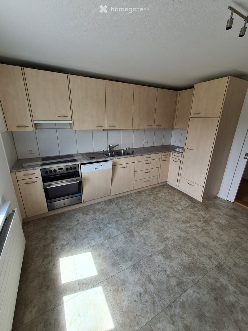 Modern kitchen with light wood cabinets, granite countertops, and stainless steel appliances including an oven and dishwasher.