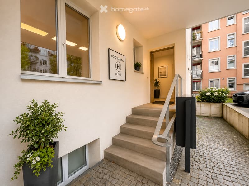 Entrance area with a staircase leading upwards, featuring a modern railing, potted plants, and a sign reading "HÖSCHGASSE 83 OFFICE".