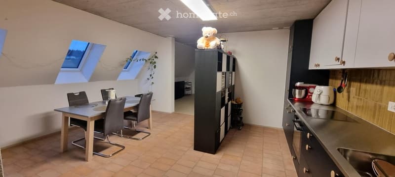 A modern kitchen and dining area with a table, chairs, a tall black cabinet, and various appliances including a mixer and oven. The space features skylight windows and a cozy teddy bear on top of the cabinet.