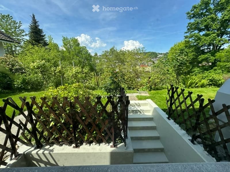 Garden area with raised ground floor, wooden fence, steps leading up, lush greenery, and trees.