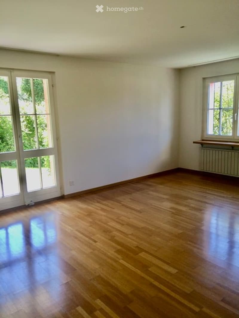 Empty room with wooden flooring, white walls, large glass door, and a window with radiator below.