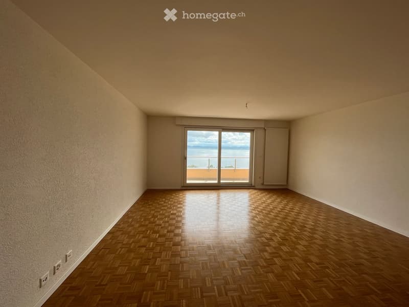 Empty room with wooden flooring, large window offering a sea view, and neutral-colored walls.