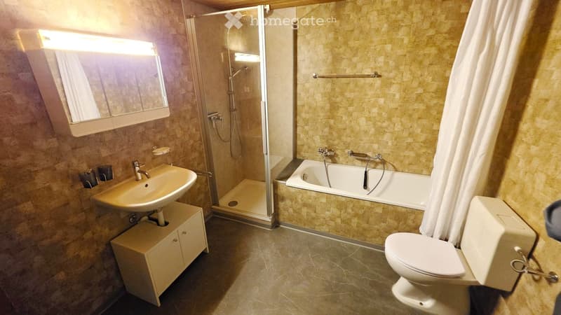 Modern bathroom with beige tiles, a sink with a mirror, a bathtub with a glass shower enclosure, and a toilet.